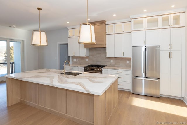 kitchen featuring light wood finished floors, decorative backsplash, appliances with stainless steel finishes, white cabinetry, and a sink