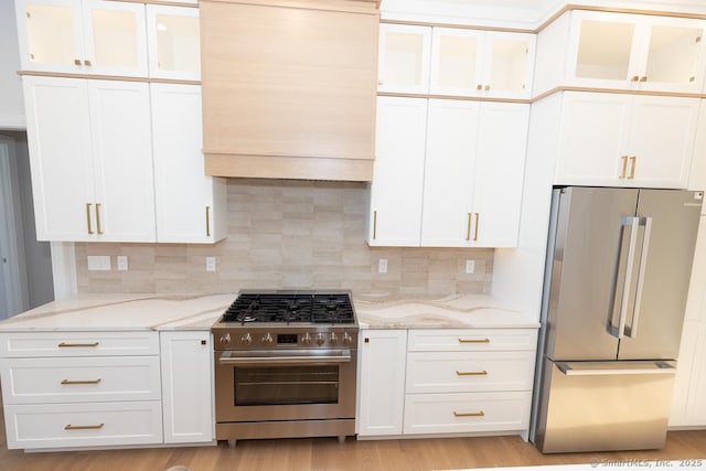 kitchen with light stone counters, white cabinetry, appliances with stainless steel finishes, light wood-type flooring, and glass insert cabinets