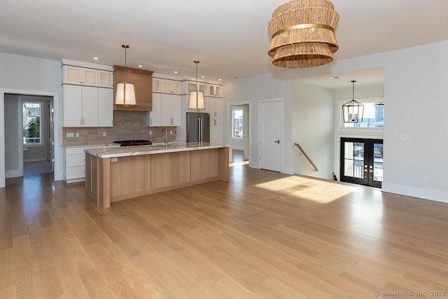 kitchen featuring a notable chandelier, light countertops, light wood-type flooring, freestanding refrigerator, and tasteful backsplash