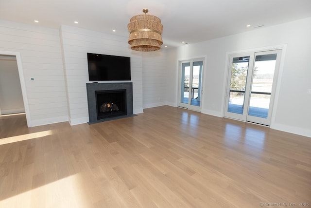 unfurnished living room featuring recessed lighting, a fireplace with flush hearth, light wood-style flooring, and baseboards