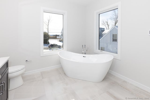 full bath featuring a healthy amount of sunlight, baseboards, a freestanding bath, and vanity