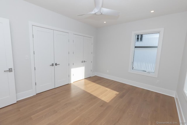 unfurnished bedroom featuring baseboards, recessed lighting, wood finished floors, and multiple closets