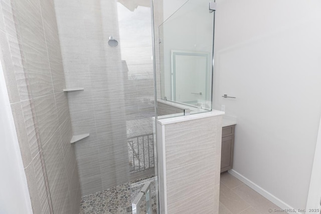 bathroom featuring tile patterned floors, a tile shower, vanity, and baseboards