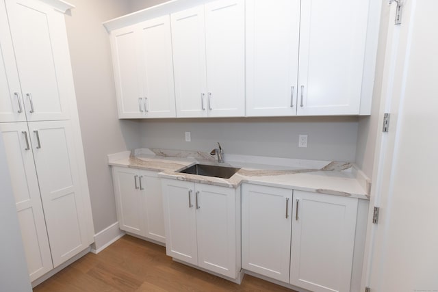 kitchen featuring baseboards, light wood finished floors, light stone counters, and white cabinets