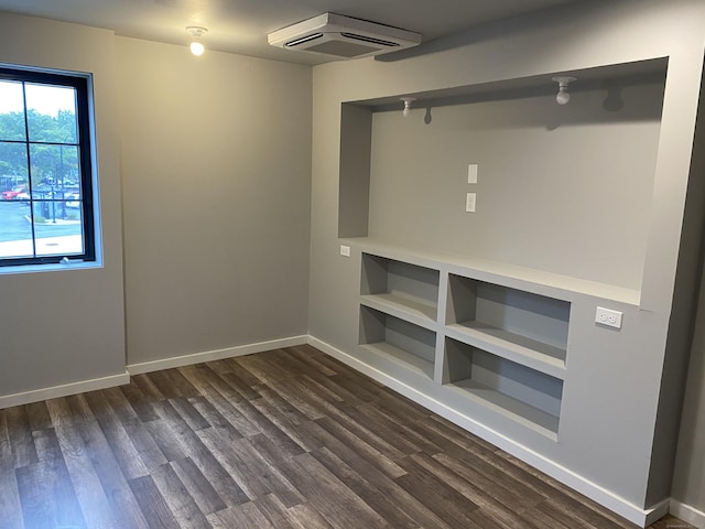 interior space with dark wood-type flooring, built in shelves, and a wall mounted AC