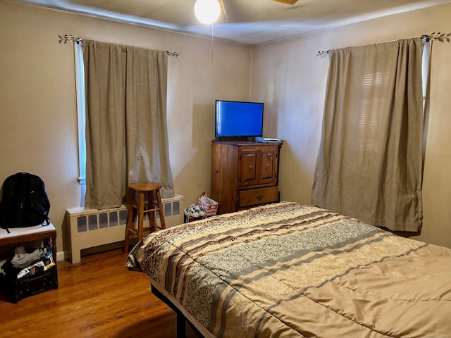 bedroom featuring wood-type flooring, radiator heating unit, and ceiling fan