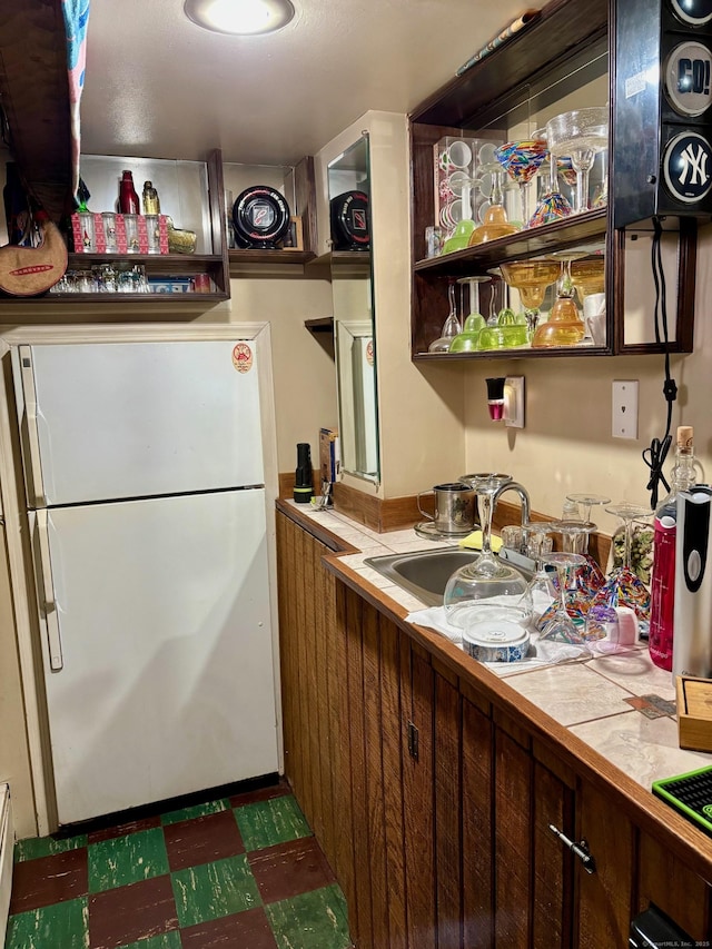 kitchen with white refrigerator, sink, tile countertops, and dark brown cabinetry