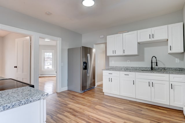 kitchen featuring stainless steel refrigerator with ice dispenser, sink, white cabinetry, baseboard heating, and light hardwood / wood-style floors