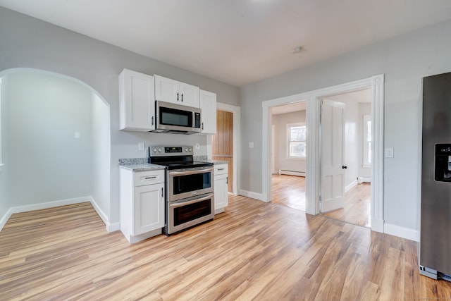 kitchen featuring white cabinetry, a baseboard heating unit, stainless steel appliances, light stone countertops, and light wood-type flooring