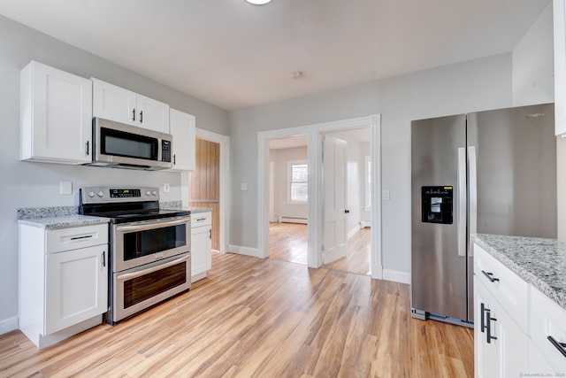 kitchen with appliances with stainless steel finishes, a baseboard heating unit, light stone countertops, white cabinets, and light wood-type flooring