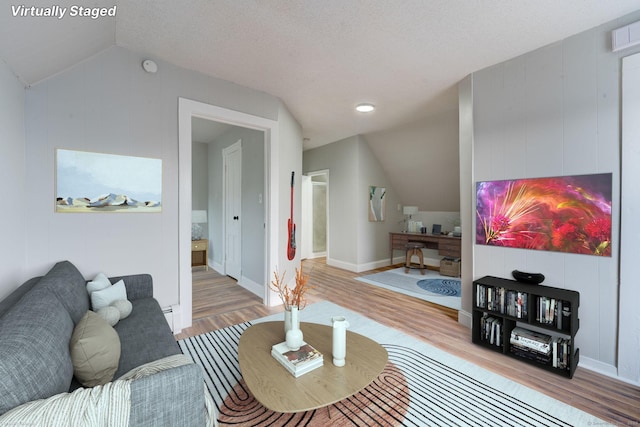 living room with vaulted ceiling, a textured ceiling, and light wood-type flooring