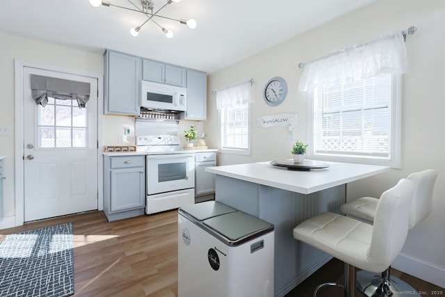 kitchen featuring an inviting chandelier, white appliances, hardwood / wood-style flooring, a breakfast bar area, and gray cabinets