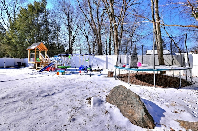 snowy yard featuring a trampoline and a playground