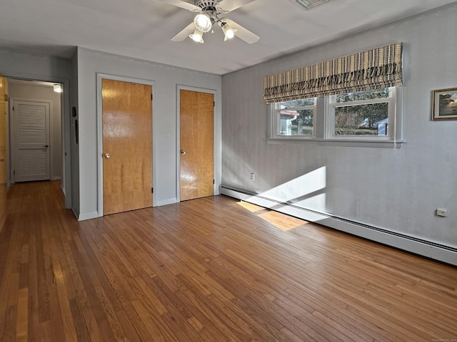 unfurnished bedroom with ceiling fan, multiple closets, a baseboard heating unit, and hardwood / wood-style floors