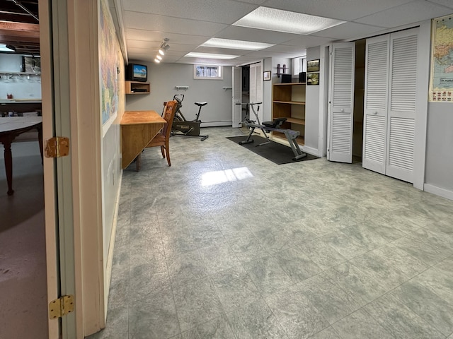 basement with a paneled ceiling and baseboard heating