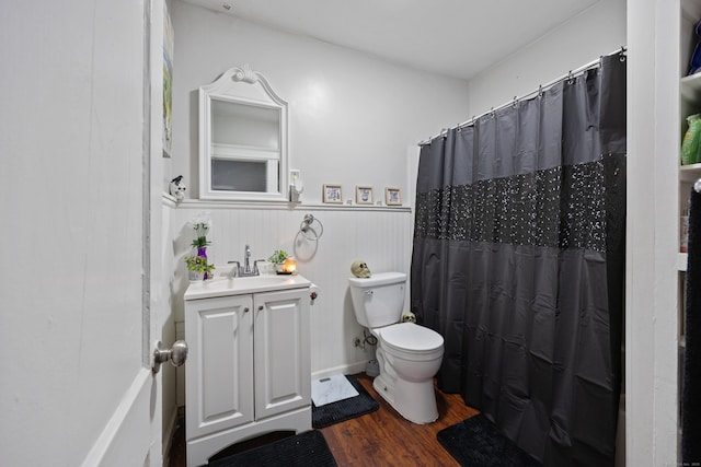 full bathroom featuring toilet, a shower with shower curtain, wood finished floors, vanity, and wainscoting