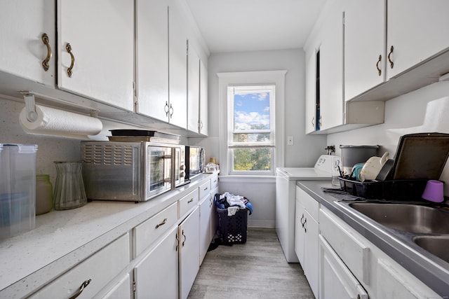 kitchen featuring light wood finished floors, light countertops, white cabinets, a sink, and washer / dryer