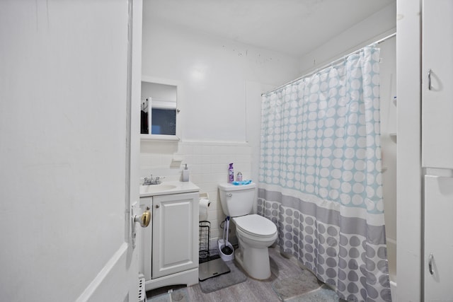 bathroom with toilet, a wainscoted wall, wood finished floors, vanity, and tile walls