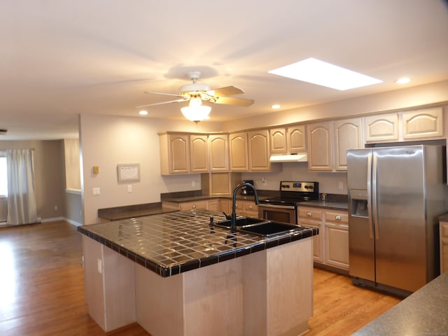 kitchen with tile counters, a skylight, stainless steel appliances, sink, and light wood-type flooring