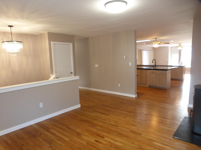 unfurnished living room with ceiling fan with notable chandelier, sink, and hardwood / wood-style floors