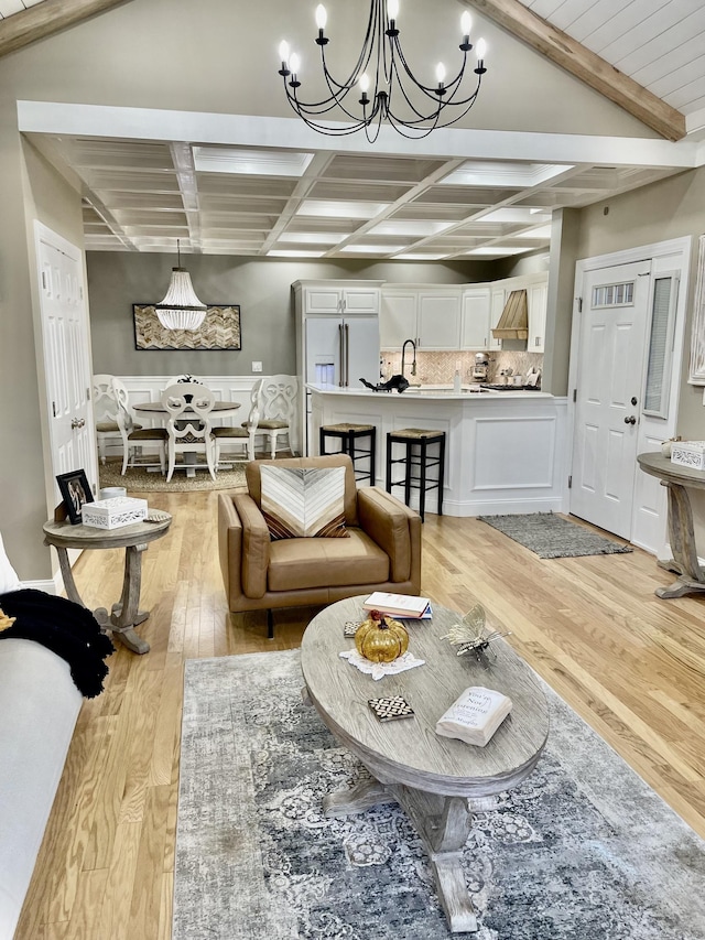 living room with beam ceiling, light hardwood / wood-style flooring, an inviting chandelier, and sink