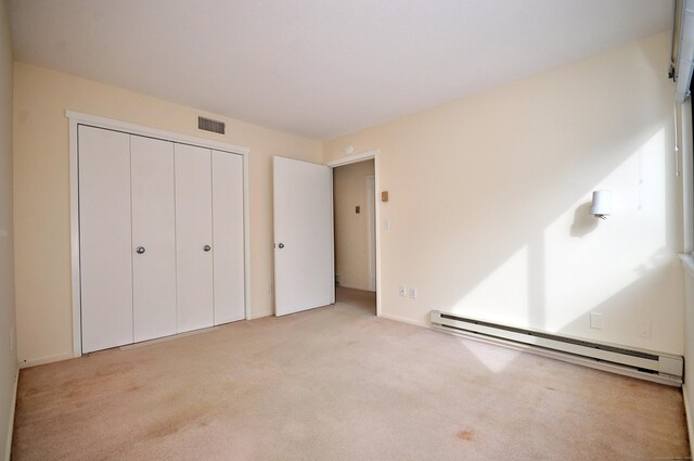 unfurnished bedroom featuring a baseboard heating unit, light colored carpet, and a closet