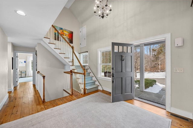 foyer featuring a towering ceiling, wood finished floors, visible vents, and a healthy amount of sunlight