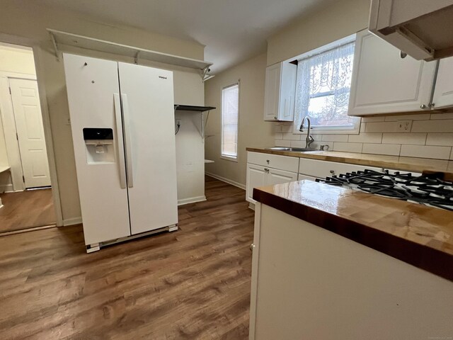 kitchen with white refrigerator with ice dispenser, butcher block counters, light hardwood / wood-style floors, white cabinetry, and sink