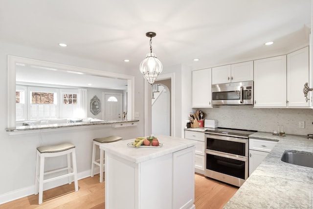 kitchen with light stone countertops, white cabinetry, appliances with stainless steel finishes, and light wood-type flooring