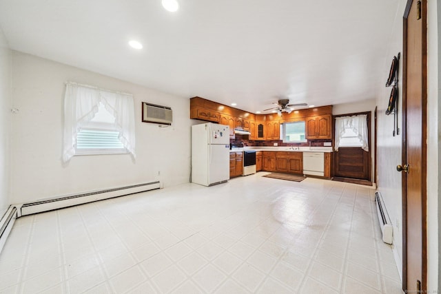 kitchen with white appliances, baseboard heating, a healthy amount of sunlight, and a wall unit AC