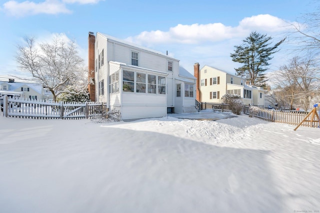 snow covered back of property with a sunroom