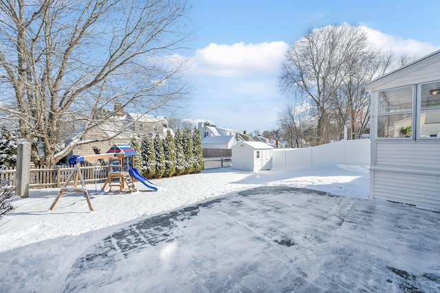 snowy yard with a storage shed and a playground