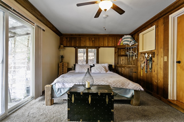 carpeted bedroom with ceiling fan, crown molding, and wooden walls