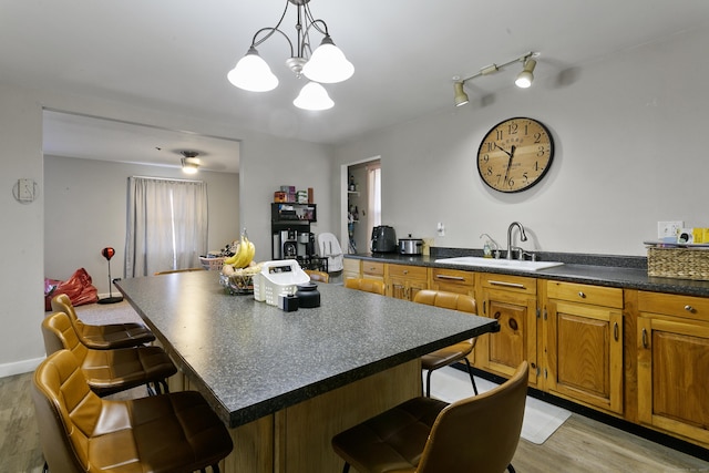 kitchen with sink, hanging light fixtures, light hardwood / wood-style flooring, a breakfast bar, and a center island