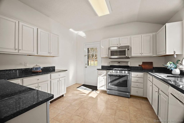 kitchen with vaulted ceiling, white cabinetry, appliances with stainless steel finishes, and dark stone counters