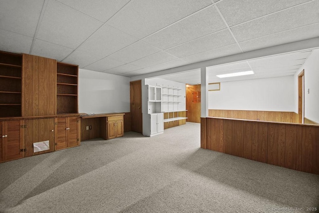 unfurnished living room with light colored carpet, wooden walls, and a drop ceiling