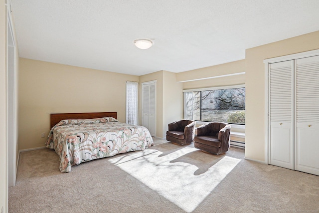 carpeted bedroom with two closets and a baseboard radiator