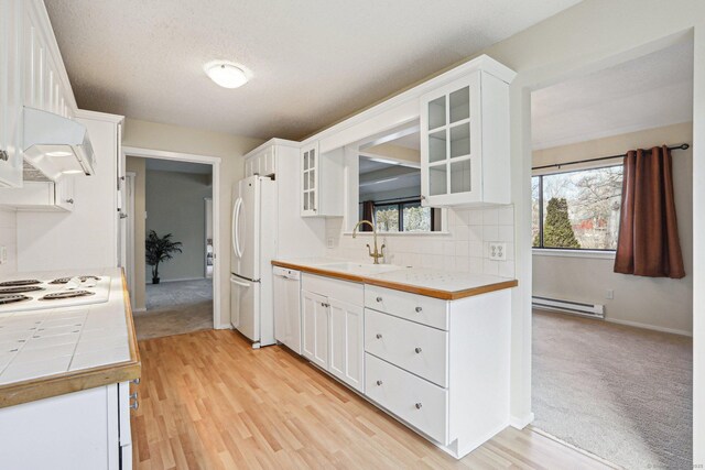 kitchen featuring white appliances, tile counters, white cabinets, a baseboard radiator, and sink