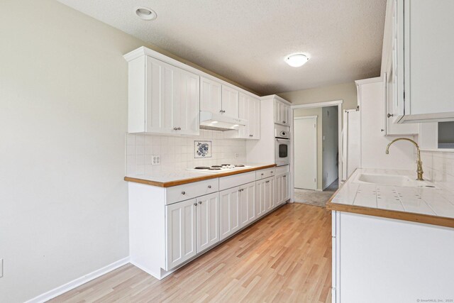 kitchen featuring sink, backsplash, white cabinets, white appliances, and light hardwood / wood-style flooring