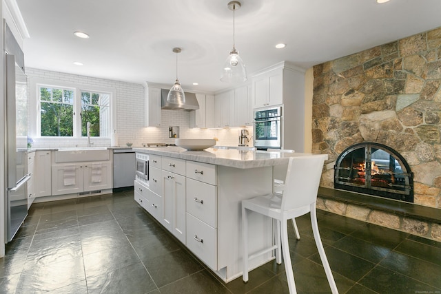 kitchen with sink, decorative light fixtures, white cabinetry, wall chimney exhaust hood, and appliances with stainless steel finishes