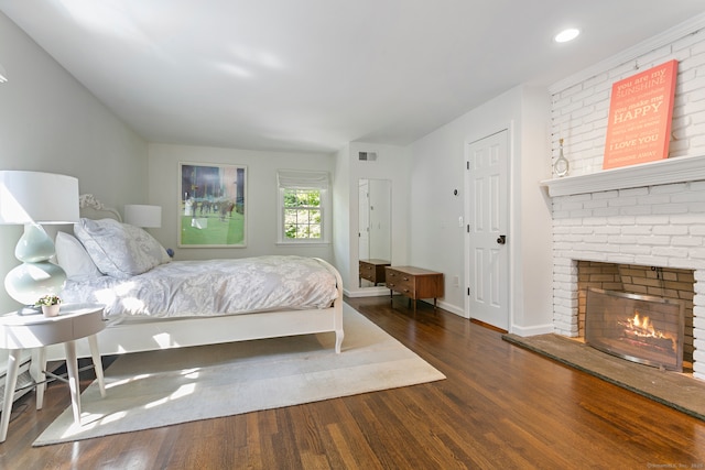 bedroom with a brick fireplace and dark hardwood / wood-style floors