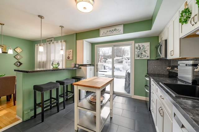 kitchen featuring white cabinets, dark tile patterned floors, decorative light fixtures, decorative backsplash, and a kitchen breakfast bar