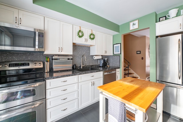 kitchen featuring appliances with stainless steel finishes, sink, backsplash, white cabinets, and dark stone countertops