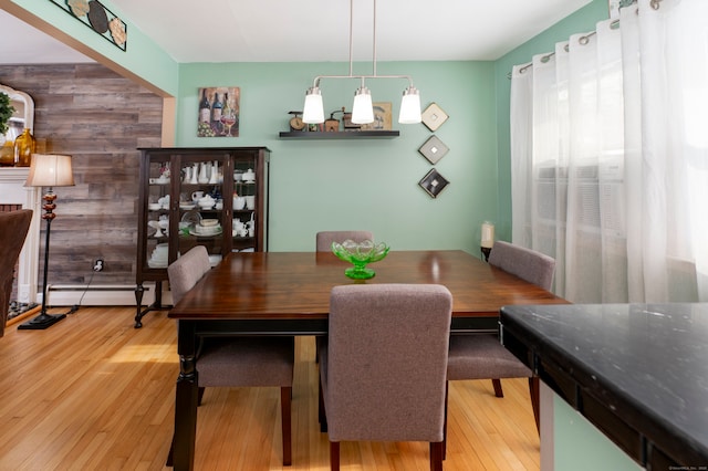 dining area featuring wood-type flooring, wood walls, and a baseboard heating unit