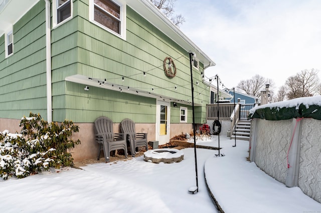 snow covered patio featuring an outdoor fire pit and a wooden deck