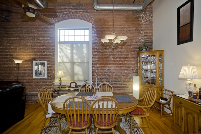 dining space featuring ceiling fan with notable chandelier, brick wall, and hardwood / wood-style floors