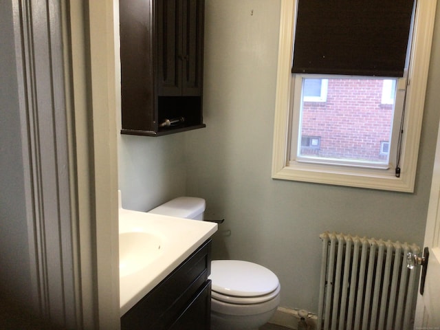 half bath with toilet, radiator heating unit, and vanity