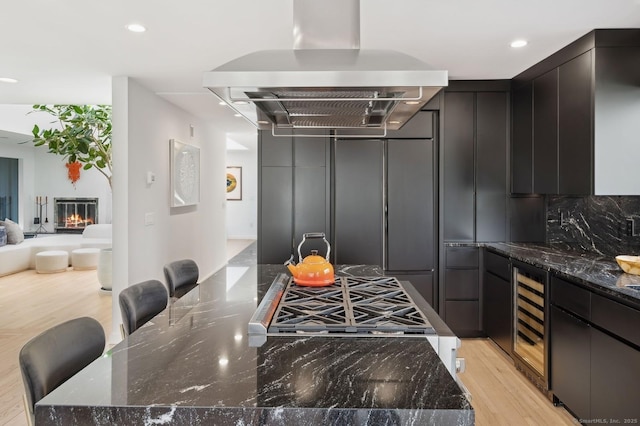 kitchen featuring island range hood, dark stone countertops, a breakfast bar, and wine cooler