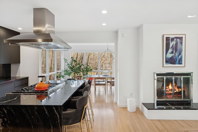 kitchen with light hardwood / wood-style floors, stainless steel gas stovetop, dark stone counters, and island range hood