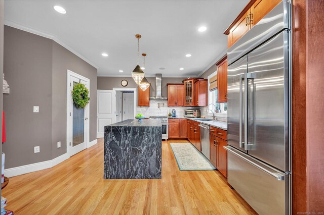 kitchen featuring wall chimney exhaust hood, dark stone countertops, hanging light fixtures, crown molding, and high quality appliances